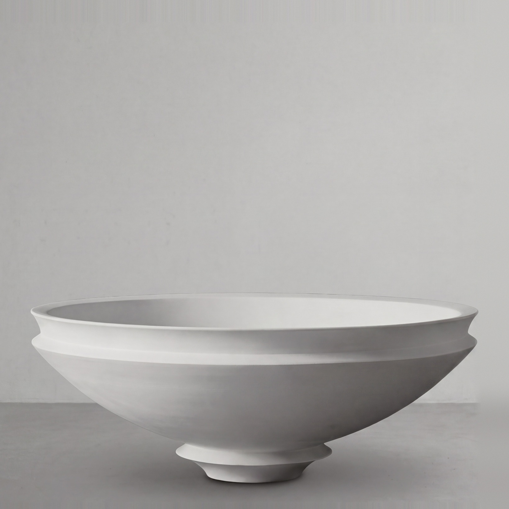 Artifact 08 in Alabaster, a wide shallow bowl, on a grey studio backdrop