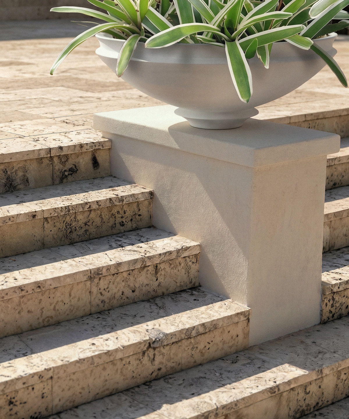 Artifact 08 planted with a variegated strap-leafed plant, set on a stone pier beside travertine steps