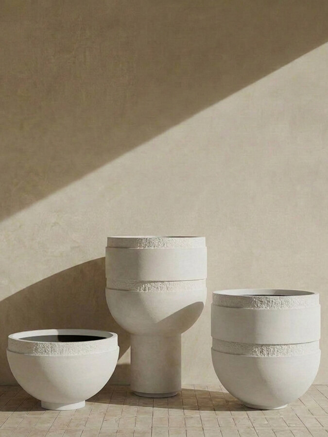 Three Orion planters in a pale finish on terracotta tile, a diagonal band of sunlight across the wall behind